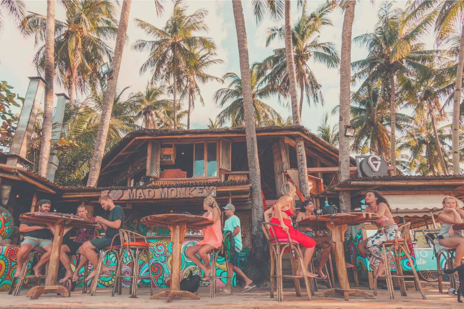 Guests at the open-air beach bar of a Mad Monkey hostel, under palm trees
