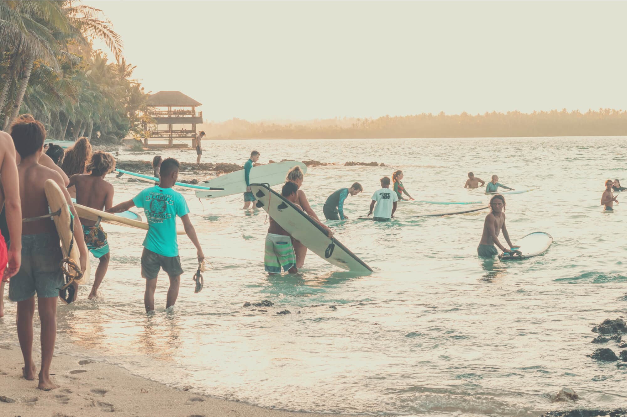 Surfers carrying boards into the water at sunset